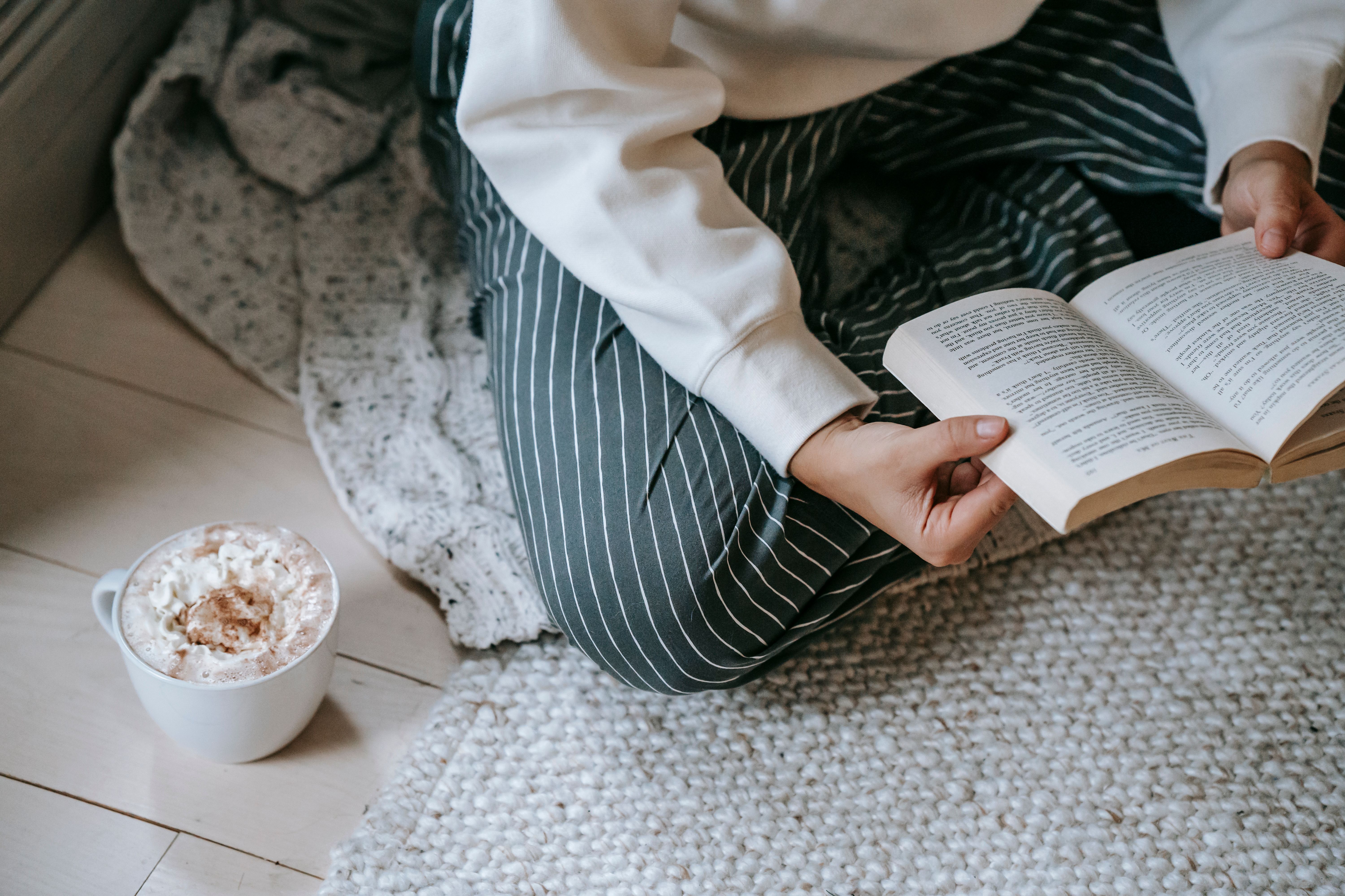 Anonymous woman sitting on a blanket reading a book with coffee, enjoying quiet private solitude